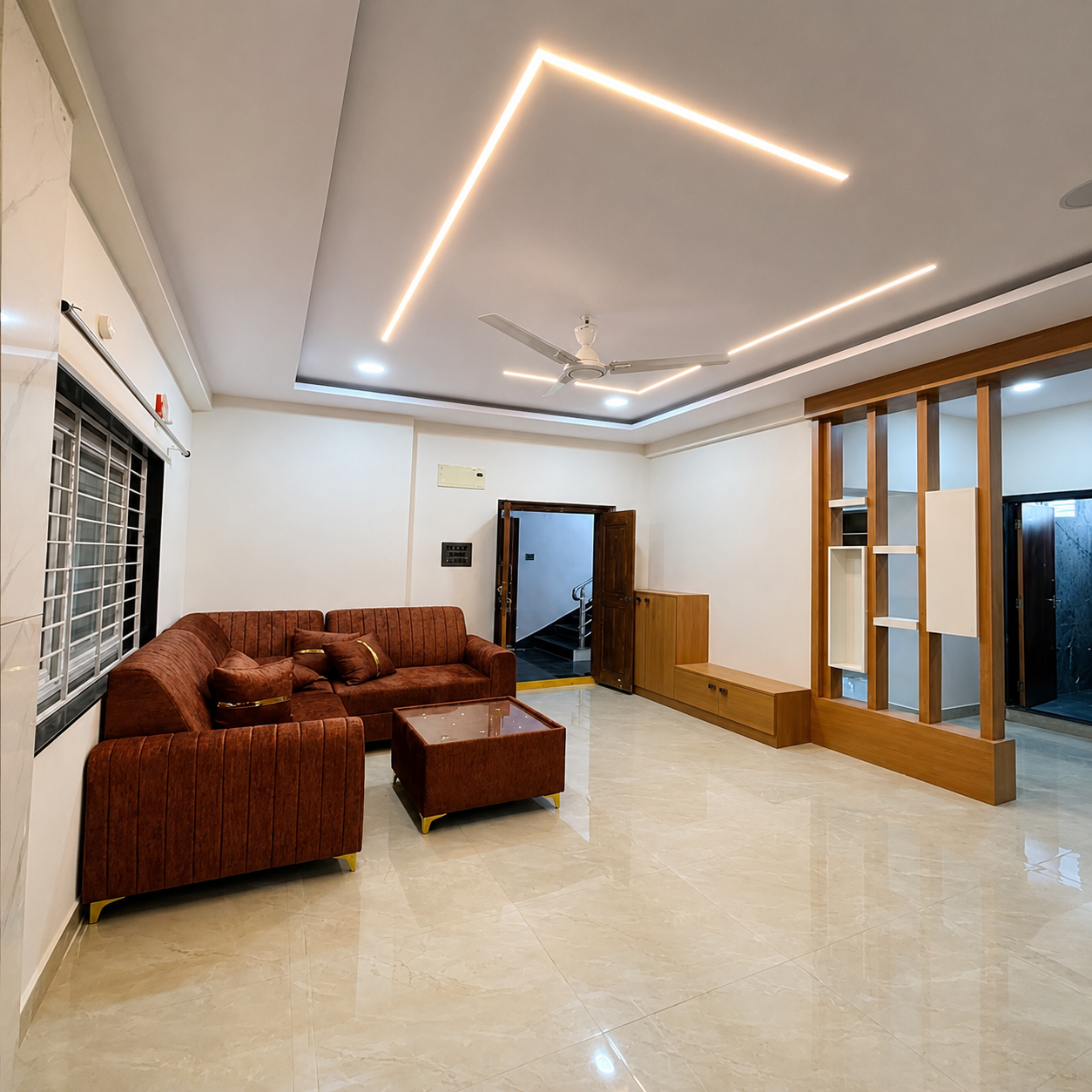 Modern living room, spacious living room, contemporary living room, stylish home interior, elegant living space, luxury living room, bright living area, open plan living, brown sofa, brown sectional sofa, comfortable sofa, upholstered sofa, modern sofa set, matching ottoman, center table, coffee table, wooden TV unit, TV wall unit, entertainment area, wooden partition, decorative room divider, wooden interior design, marble flooring, glossy floor, polished flooring, false ceiling, modern ceiling design, LED strip lighting, ambient lighting, recessed lighting, ceiling fan, large window, natural light, airy living room, clean interior, organized home, minimalist interior, modern apartment, residential interior, urban home design, student-friendly accommodation, student living space, student rental home, study-friendly home, working professional accommodation, professional living space, work-life balance home, comfortable rental property, family-friendly living room, real estate interior.